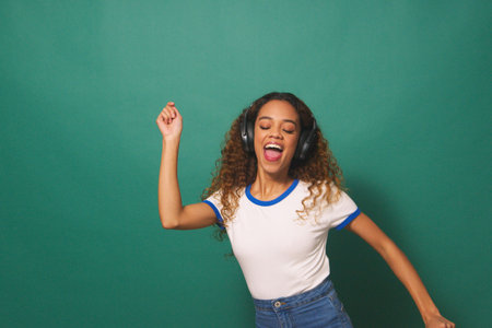 Wide shot, young biracial woman dancing with headphones, green studio backgroundの写真素材