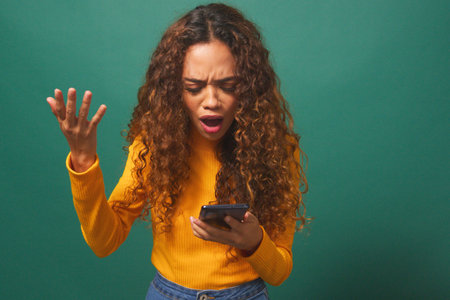 Young biracial woman reads text message shocked wow, green studio background