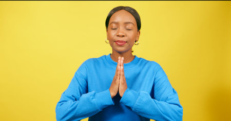 Calm young woman puts hands into prayer position, praying, yellow studioの写真素材
