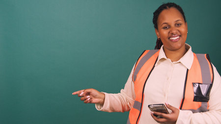 Young Black construction worker points to copy space smiling, working on site