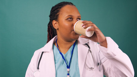 Young Black female doctor drinks coffee from takeaway cupの写真素材
