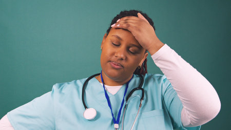 Tired young Black doctor rubs forehead and sighs, end of surgery