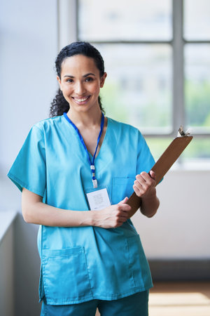 Smiling Female Doctor Holding Clipboard in Bright Hospital Corridorの写真素材