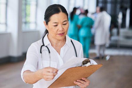 Focused Female Doctor Reviewing Patient Information in a Modern Hospitalの写真素材