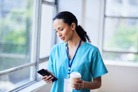 Focused Doctor Checking Phone While Holding Coffee in the Hospitalの写真素材
