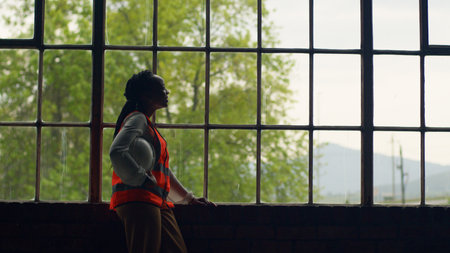 Female Engineer Reflecting By Window In Construction Setting With Safety Gear