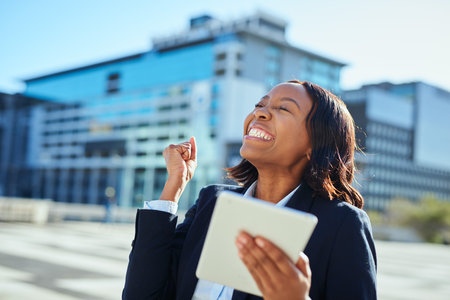 Happy Businesswoman Celebrating Success with Digital Tablet in Urban City Environmentの写真素材