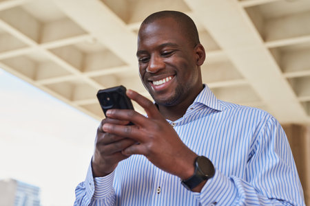 Smiling Man Engaged with Smartphone in Urban Settingの写真素材