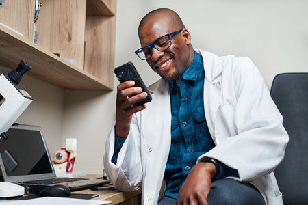 Smiling Optometrist in White Coat Holding Smartphone in Modern Office Environment