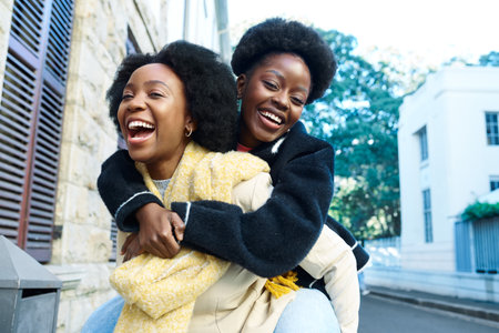 Joyful Young Women Piggybacking Each Other on a City Street Laughing and Enjoying Friendship on a...