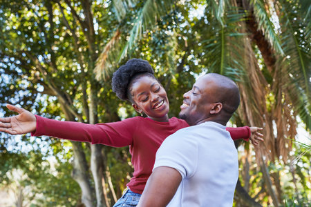 Joyful Couple Embracing in a Sunlit Park Under Tropical Trees in the Cityの写真素材