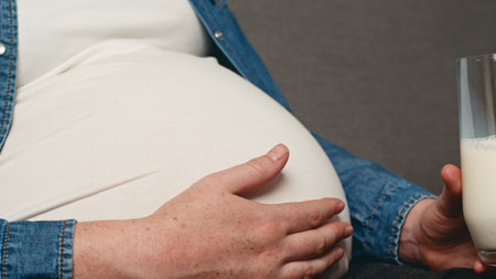 Pregnant Woman Relaxing With Glass of Milk and Hand on Belly in Comfortable Settingの写真素材