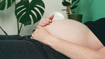 Expectant Mother Gently Cradles Her Baby Bump at Home in a Comfortable Setting With Lush Greeneryの写真素材