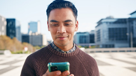 Young Man Smiling While Using Smartphone Outdoors in the City