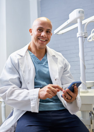 Friendly Smiling Male Dentist in a Clinic Setting Using a Smartphone