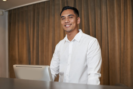 Smiling Professional in White Shirt Standing by Computer in Modern Interiorの写真素材