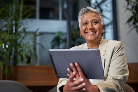 Confident Senior Woman Smiling While Using a Digital Tablet in a Modern Workplace Setupの写真素材