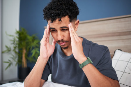 Young Man Sitting on Bed Showing Signs of Stress or Discomfortの写真素材