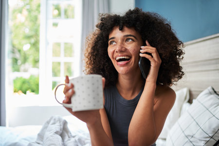 Woman Smiling While Talking on the Phone and Holding a Polka Dot Mug at Homeの写真素材