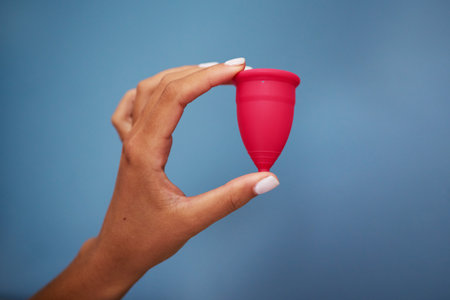Close-Up of Hand Holding Pink Menstrual Cup Against Blue Background for Feminine Health and Sustainabilityの写真素材