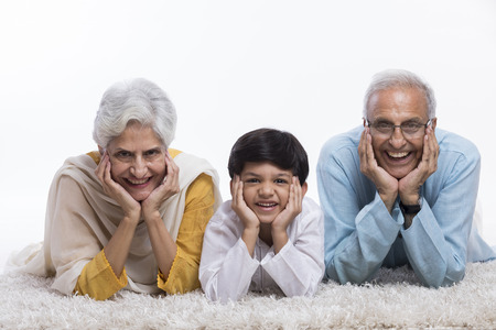 Grandparents and grandson lying on carpet with hand on chinの写真素材