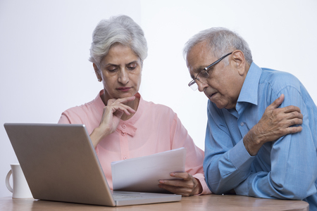 Senior couple looking at documents with laptop sitting on tableの写真素材