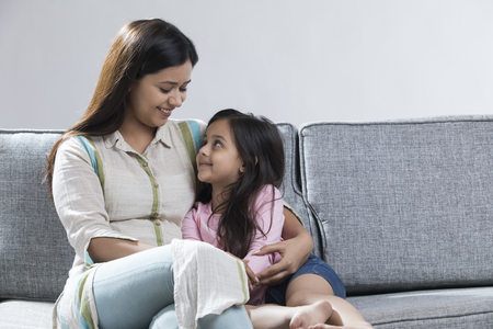 Smiling mother and daughter sitting together on sofaの写真素材