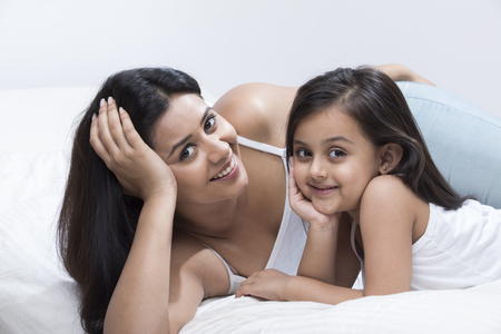 Mother and daughter lying on bed with hand on chinの写真素材