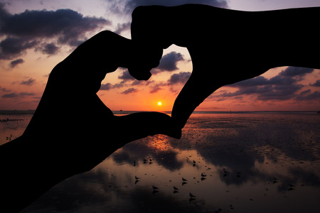 Silhouette hand in heart shape with sunriseの写真素材