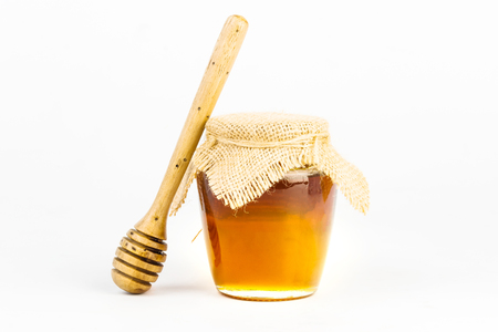 Glass jar full of honey wooden honey dipper on white backgroundの写真素材