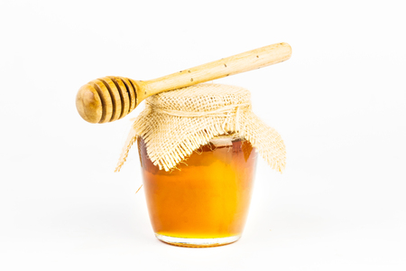 Glass jar full of honey wooden honey dipper on white backgroundの写真素材
