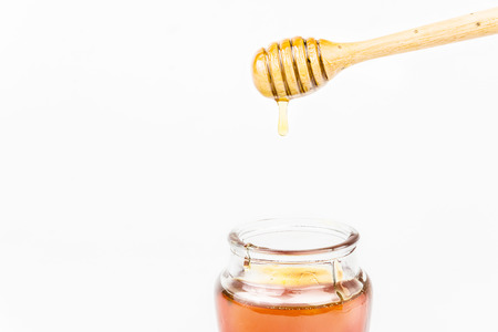 Glass jar full of honey wooden honey dipper on white backgroundの写真素材
