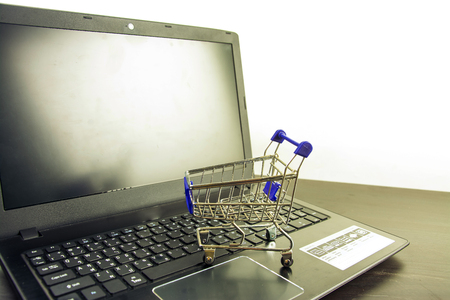 Computer notebook blank screen with shopping cart on wood tableの写真素材
