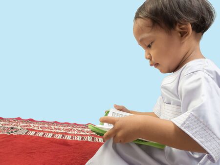Muslim boy in a dress  reading the Koran , isolate background .の写真素材