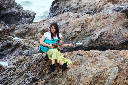 Beautiful asian woman with a guitar on rockの写真素材