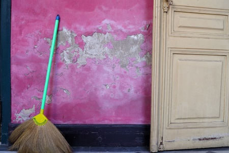 Broom leaning against a grunge pink wall 