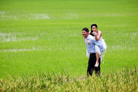 Smiling groom carrying on his back bride in paddy fieldの写真素材