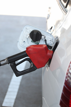 Red fuel nozzle in pouring to car on gas station.の写真素材