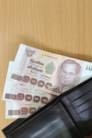 Banknotes of Thailand in wallet on wood background.