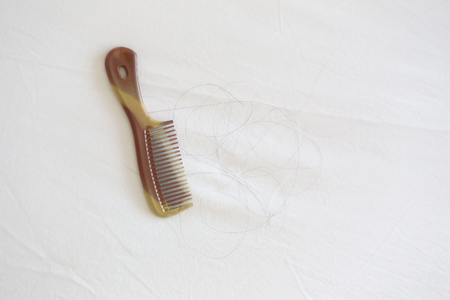 Comb and black hair of women placed on white cloth in the concept problem of hair loss.