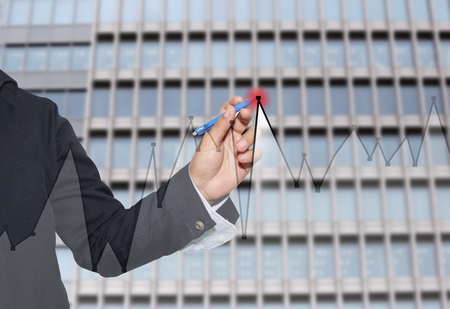 Hand of businessman drawing graphics a top point growing graph to concept of profit in business and have skyscraper background.の写真素材