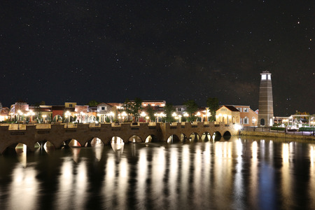 Scenery of the river bridge into the village at night with bright lights and have Milky Way on dark sky.の写真素材