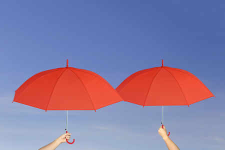 Red umbrella in hand on blue sky background concept of sun protection.の写真素材