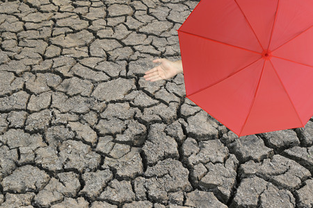 Red umbrella and a hand of man standing on cracked earth and hand protruding outside the radius to determine whether it rains or not,concept of risks in business and nature aridity.の写真素材