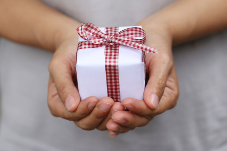 White Gift box on hand and Red Ribbon on gift box,Concept christmas Day and New Year,small gift box in hand.の写真素材