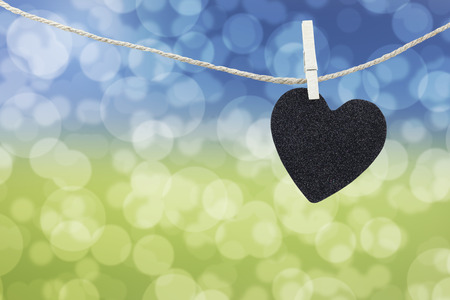 Black Heart hung on hemp rope on abstract colorful bokeh background and have copy space to manage the text you want.の写真素材