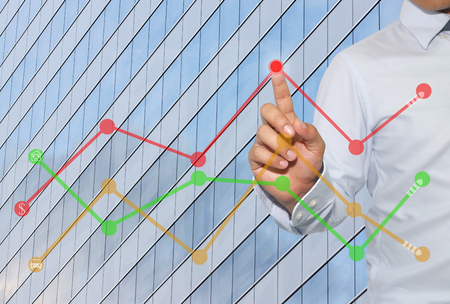 Finger of businessman touch to the peak of business graph on Skyscraper background,concept to success and profitability.の写真素材