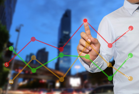 Finger of businessman touch to the peak of business graph on Skyscraper background,concept to success and profitability.の写真素材