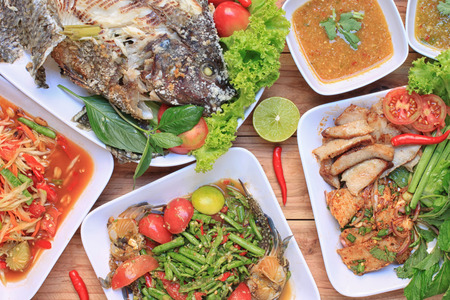 Collection of thai food on wood floor,papaya salad (SOM TUM),Spicy Grilled Pork Salad and Grilled Fish in the food has been popular in Thailand.の写真素材