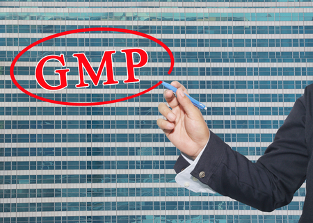 hand of a business man use a pen write text system GMP on glass wall of tall building background.の写真素材